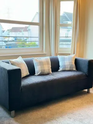 a blue couch with pillows in front of a window at Kingfisher Apartment in Dunfermline