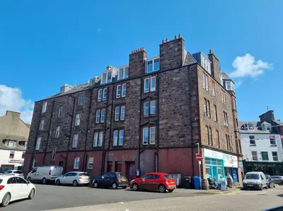 a large brick building with cars parked in front of it at Mafeking Place Apartment in Campbeltown