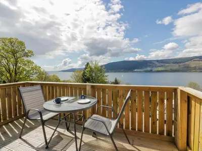 a table and chairs on a deck with a view of a lake at 11A Mansion View in Helensburgh