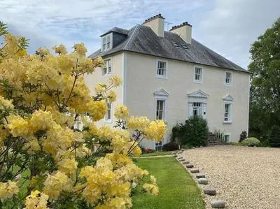 a large white house with yellow flowers in front of it at Country Home on Private Estate in Minishant