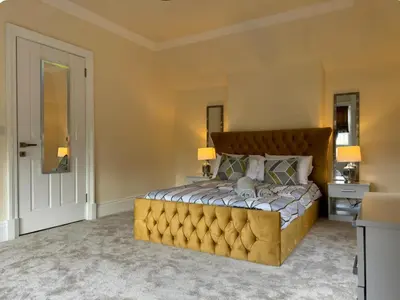 a bedroom with a large bed with a yellow tufted headboard at 3 Bed - Sleeps 7 - Free Parking - Central Location in Glasgow