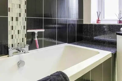 a white bath tub in a bathroom with black tiles at Blackness Apartment in Linlithgow