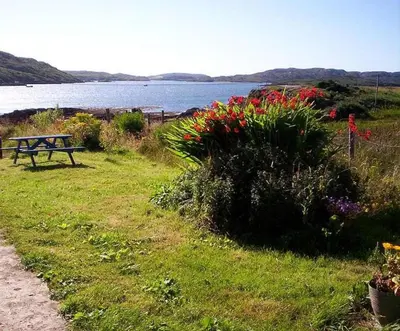 a park bench sitting next to a lake with flowers at Cottage-IsleofMull-StunningViews-WiFi-Parking in Bunessan
