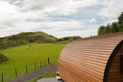 a wooden building with a hill in the background at Countryside Farm Pod on Isle of Seil - A in Balvicar