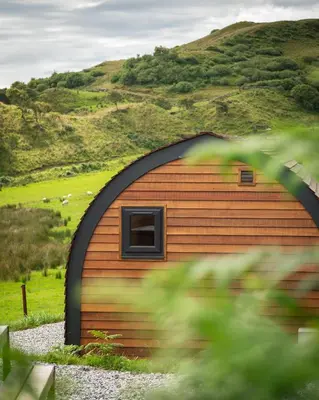 a small wooden building with a hill in the background at Countryside Farm Pod on Isle of Seil - A in Balvicar