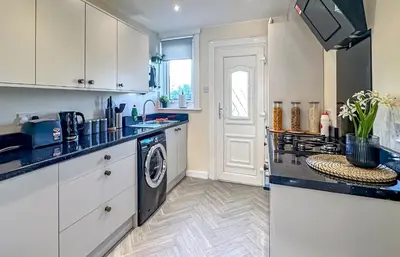 a kitchen with white cabinets and a washer and dryer at Colourful life-house near Glasgow in Clydebank