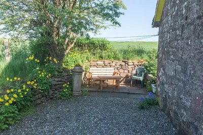 a garden with a bench and a stone wall at Ballat Smithy Cottage in Drymen