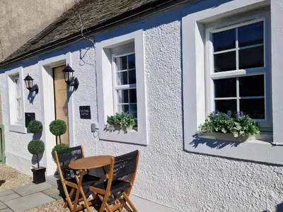 a table and chairs outside of a house with windows at Lyne Cottage, The Retreat in West Linton