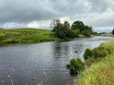 a river in a field next to a grassy field at Ryehill with Fishing in Sanquhar