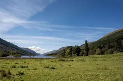 a grassy field with a lake and mountains in the background at Bruach in Balquhidder