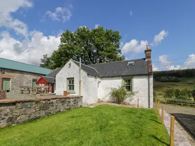 a white cottage with a stone wall and a yard at Kilnmark Farmhouse in Thornhill