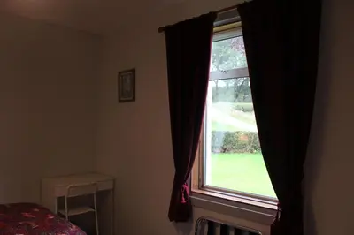 a bedroom window with a view of a green yard at Lednabra Cottage in Drymen