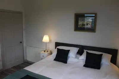 a bedroom with a white bed with two green pillows at Lednabra Cottage in Drymen