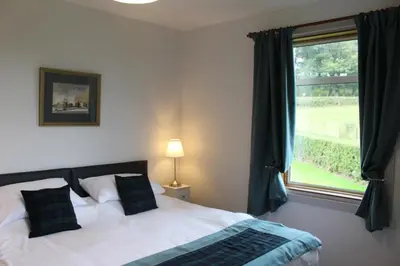 a bedroom with a bed and a large window at Lednabra Cottage in Drymen