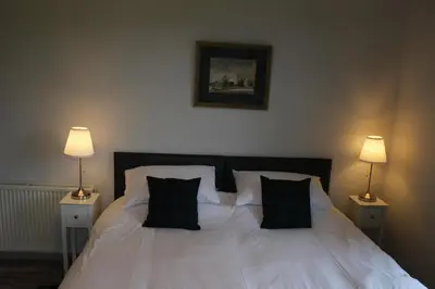 a bedroom with a white bed with black pillows at Lednabra Cottage in Drymen