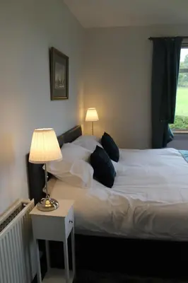 a bedroom with a bed with pillows and a lamp at Lednabra Cottage in Drymen