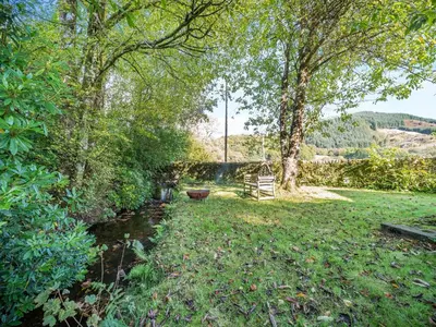 a yard with a stream and trees and a bench at North Lodge in Colintraive