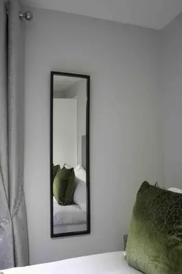 a mirror on a white wall next to a bed at Pentland House in Bathgate