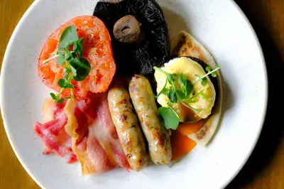 a plate of food with sausage potatoes tomatoes and toast at Luss Cottages at Loch Lomond Arms Hotel in Luss