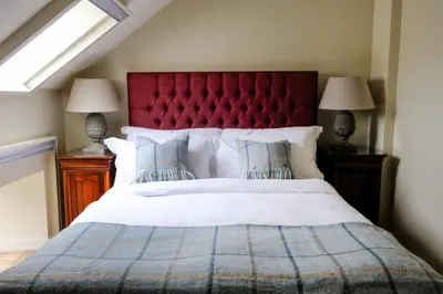a bedroom with a large bed with a red headboard at Luss Cottages at Loch Lomond Arms Hotel in Luss