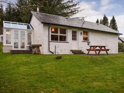 a small white house with a picnic table in the yard at Pine Cottage in Killin