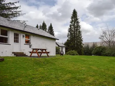 a white house with a picnic table in a yard at Pine Cottage in Killin