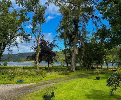 a path through a park with trees and a lake at The Coach House Knipoch in Oban