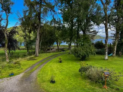 a dirt road through a field with trees and water at The Coach House Knipoch in Oban