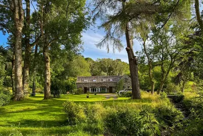a house in the middle of a field with trees at The Coach House Knipoch in Oban