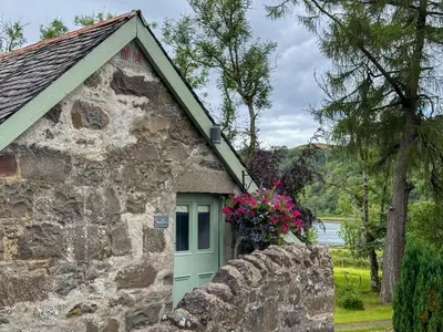 a stone building with a green door and flowers at The Coach House Knipoch in Oban