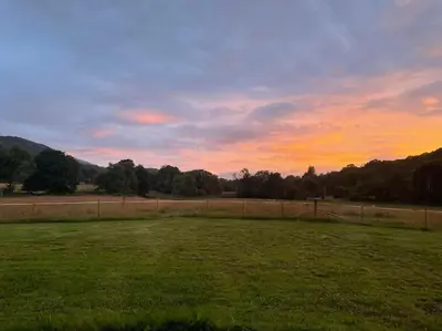a field with a fence and a sunset in the background at Riverview Lodge & Luxury Hot Tub in Acharra