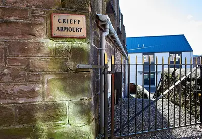a sign on the side of a building with a fence at Crieff Armoury in Crieff