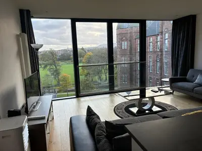 a living room with a couch and a large window at Executive Quartermile apartment near to Castle University with park view in Edinburgh