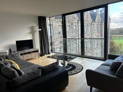 a living room with a couch and a large window at Executive Quartermile apartment near to Castle University with park view in Edinburgh