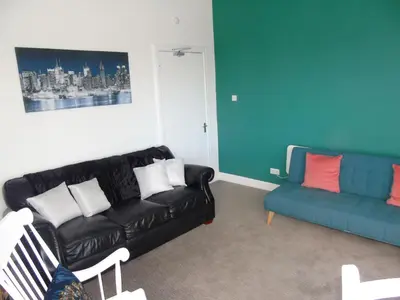 a living room with a black leather couch and a blue couch at Snug - Grian-aig Apartment in Greenock