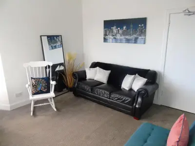 a living room with a black leather couch and a chair at Snug - Grian-aig Apartment in Greenock