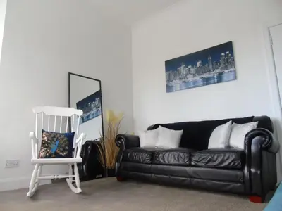 a black couch and a white chair in a living room at Snug - Grian-aig Apartment in Greenock