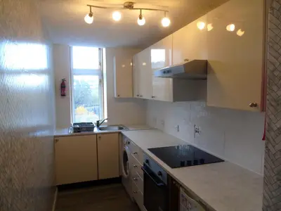 a kitchen with white cabinets and a sink and a stove at Snug - Grian-aig Apartment in Greenock