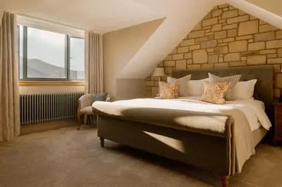a bedroom with a large bed and a brick wall at Brenachoile Cottage in Callander
