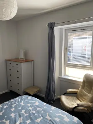 a bedroom with a bed and a chair and a window at Garden flat in Largs