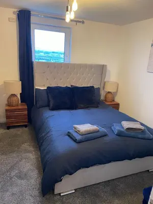 a bedroom with a large bed with blue sheets and a window at Harbour bliss in Ardrossan