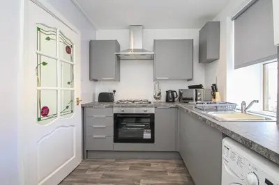 a kitchen with white cabinets and a stove top oven at Tobago Urban Apartment in Greenock