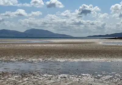 a beach with rocks and water with mountains in the background at Old Powdermill Cottage in Tighnabruaich
