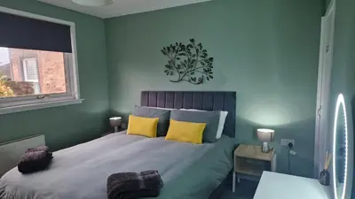 a green bedroom with a bed with yellow pillows at 175 On Clyde - Spacious & Cosy Cedar Wood Bungalow in Helensburgh