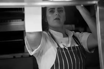 a woman in an apron standing in front of an oven at Angels Hotel in Uddingston