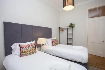 two beds in a room with white walls at Lovely Flat in Ideal Location in Glasgow