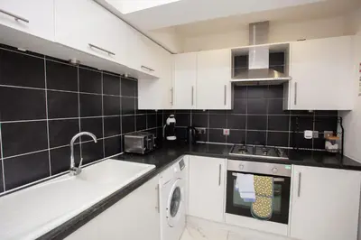 a kitchen with white cabinets and black tiles at Beautiful 2 Bed Flat with a Private Terrace in Glasgow