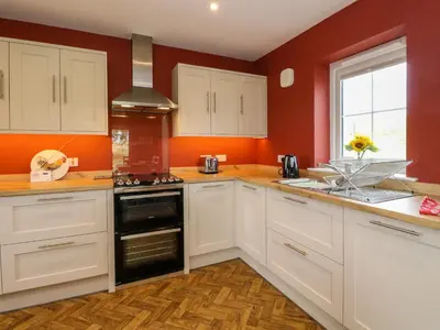 a kitchen with white cabinets and an orange wall at Tirlaggan Úr in Oban