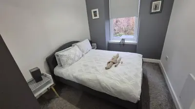 a teddy bear laying on a bed in a bedroom at Bellshill Central Apartment in Bellshill