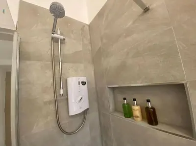 a shower with a shower head and two bottles on a shelf at 1 Smithhills Sleeps 5 Central and Spacious in Paisley